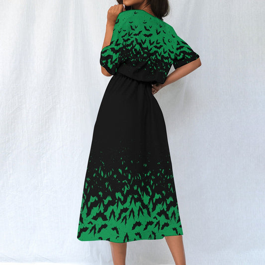 An elegant woman standing and posing in a spooky green and black bat-patterned blouson dress with elastic waist and pockets, accessorized with black boots and a black belt.