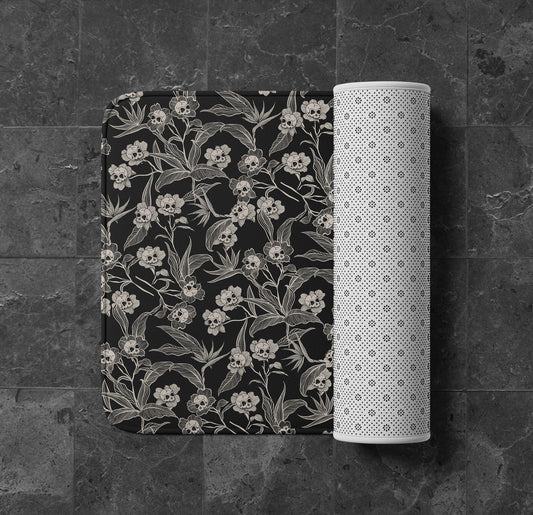 an elegant yet spooky gothic floral skull flower memory foam bath mat in black and cream on a black granite tile floor. 
