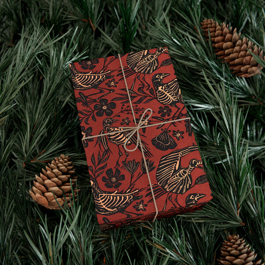 Gift box with red and black floral bird skeleton patterned wrapping paper on green foliage with pine cones
