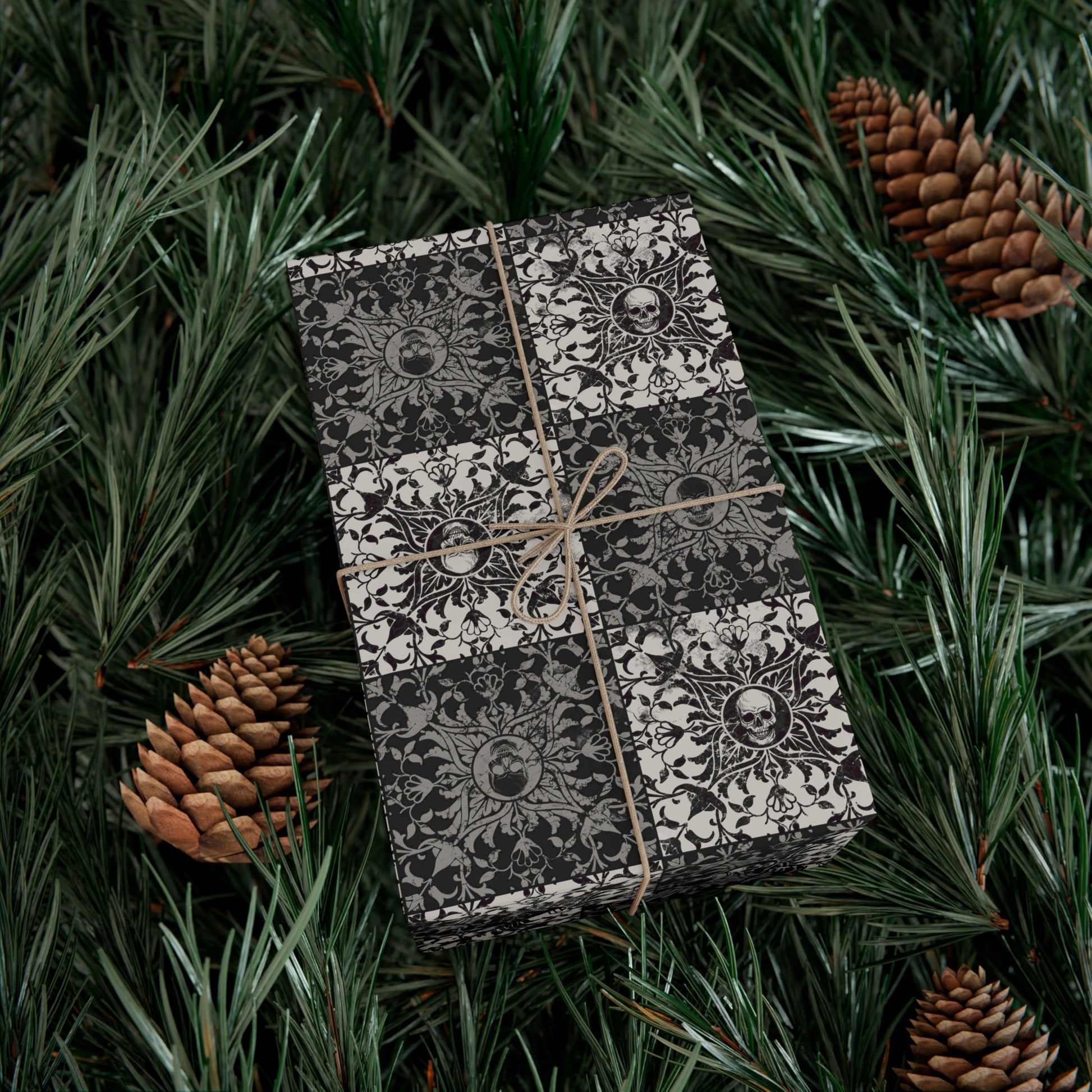 Gift box with skull pattern wrapped in paper and tied with string, surrounded by pine branches and pinecones.