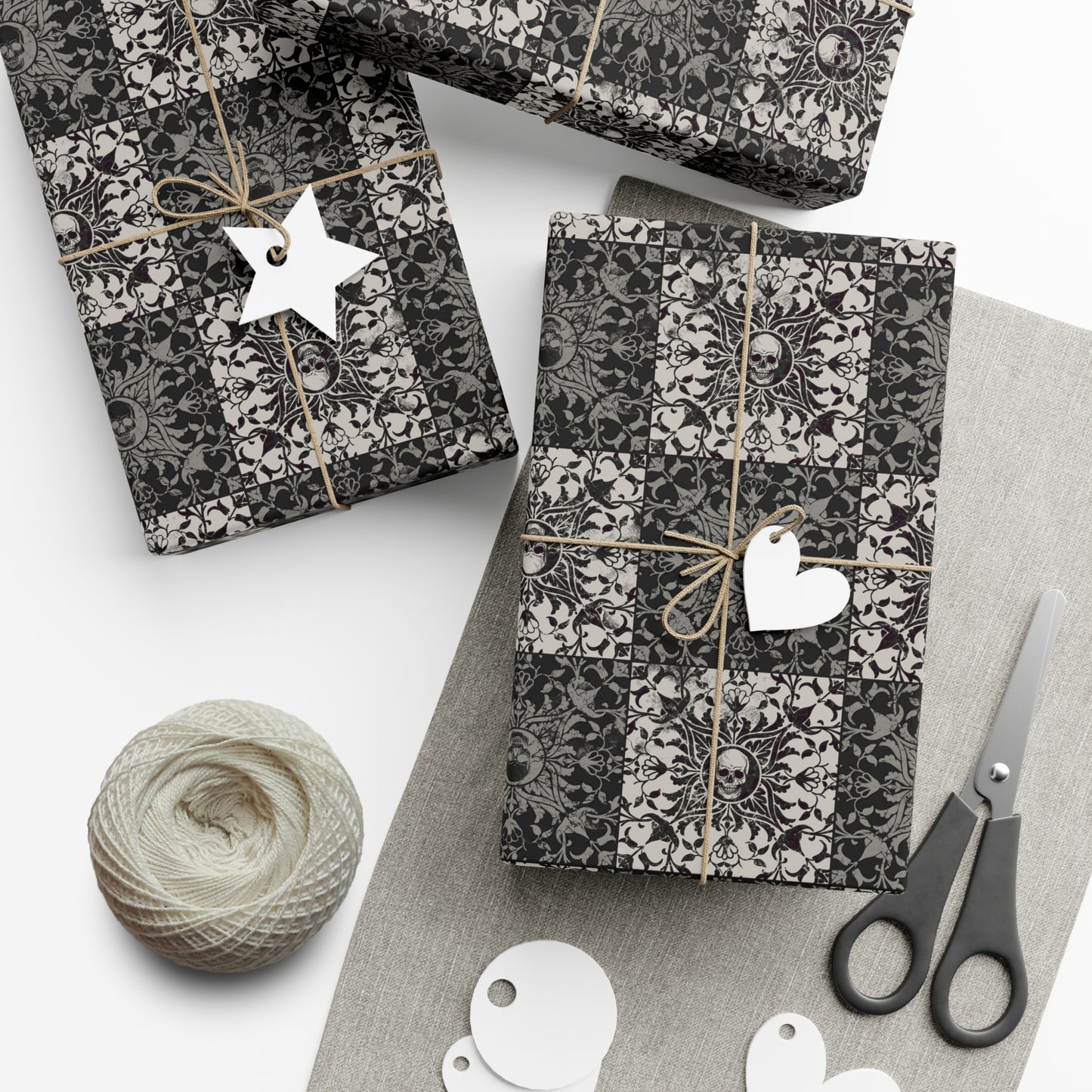 Gift boxes wrapped in black and white gothic patterned paper with decorative tags and scissors on a light surface.