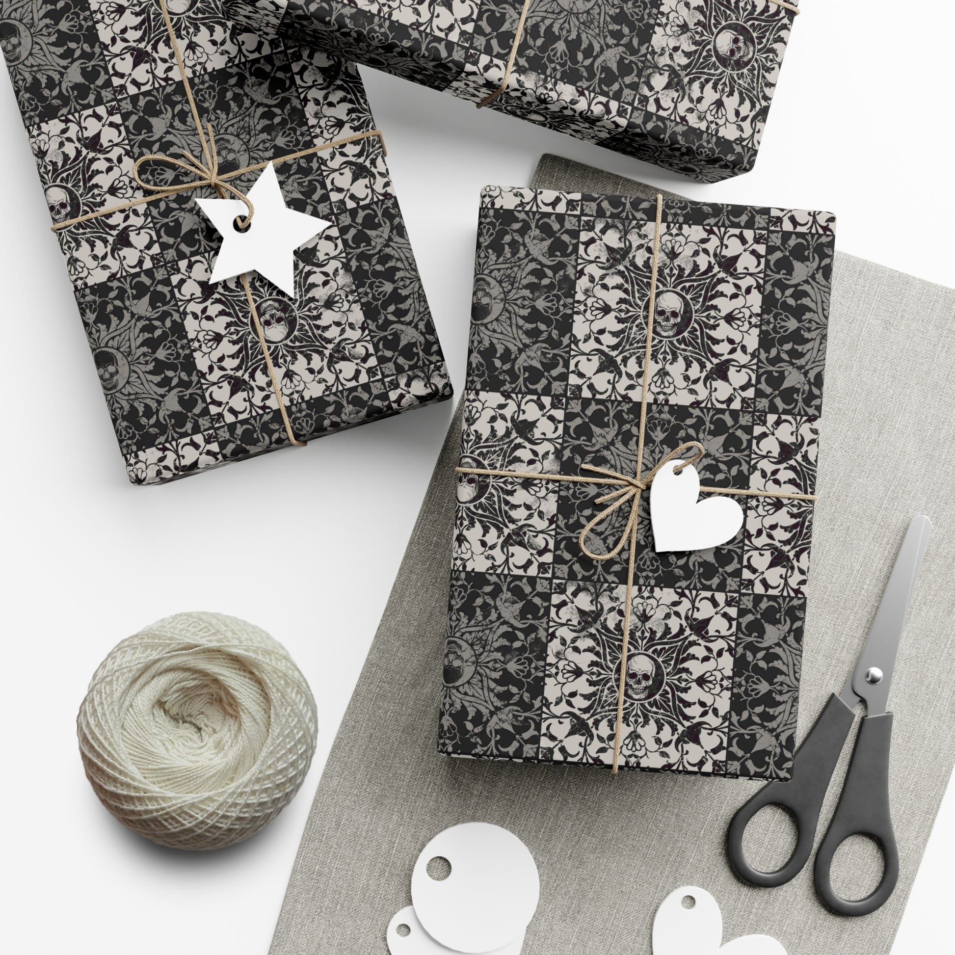 Gift boxes wrapped in black and white gothic patterned paper with decorative tags and scissors on a light surface.