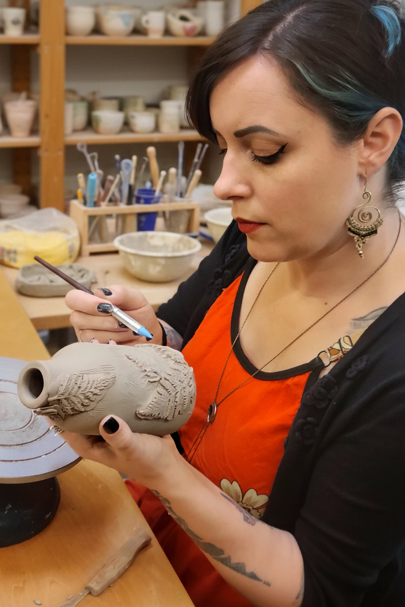 Person working on a ceramic vase with a brush in a workshop setting