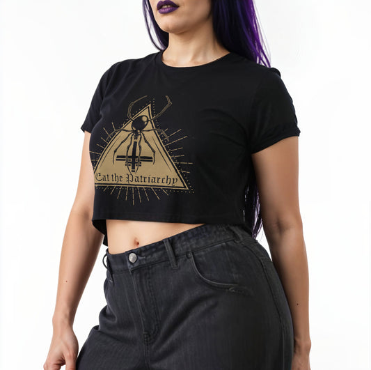 Person wearing a black crop top with a black widow design and text stating "eat the patriarchy", standing against a white background