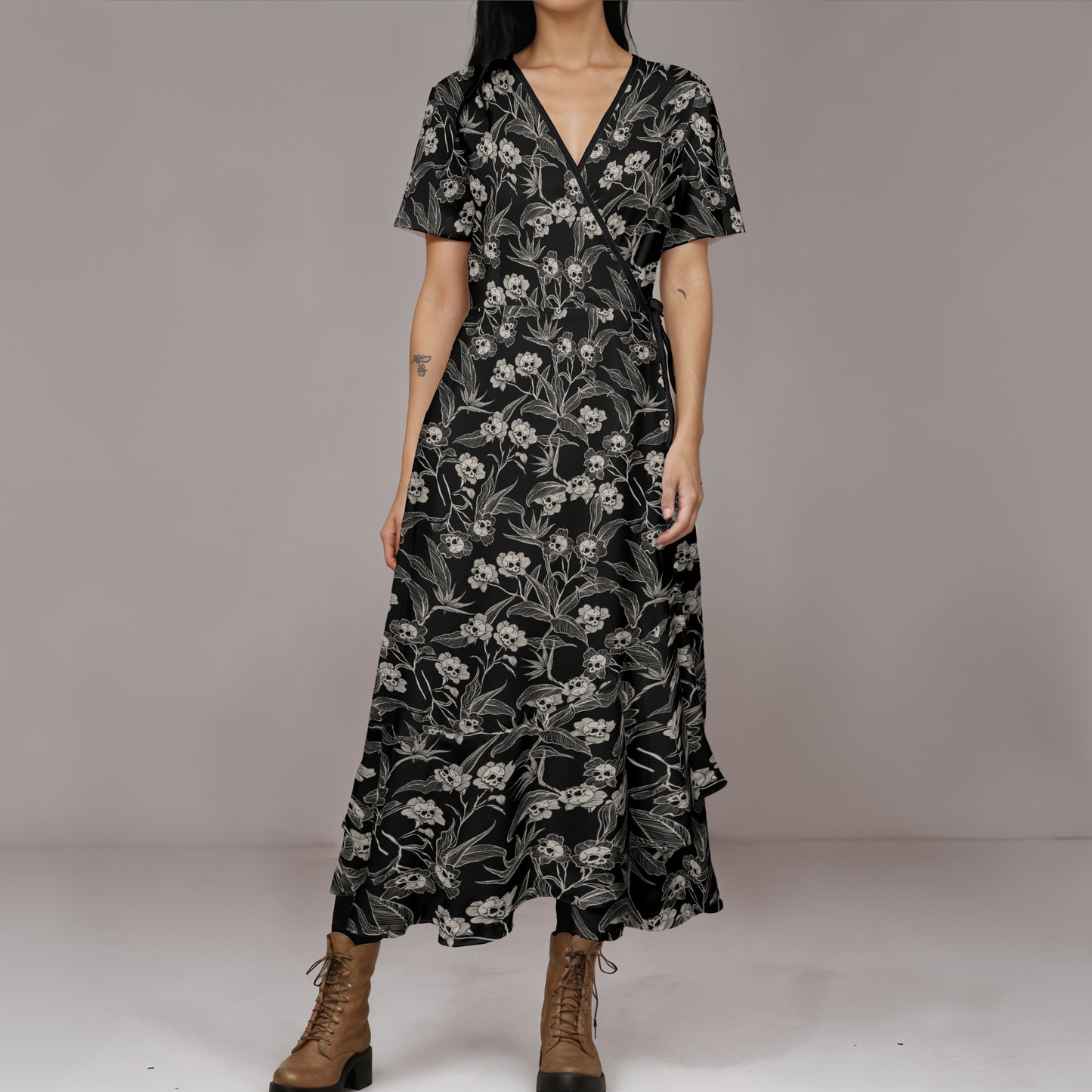 Woman wearing a black gothic floral dress with brown boots on a plain background