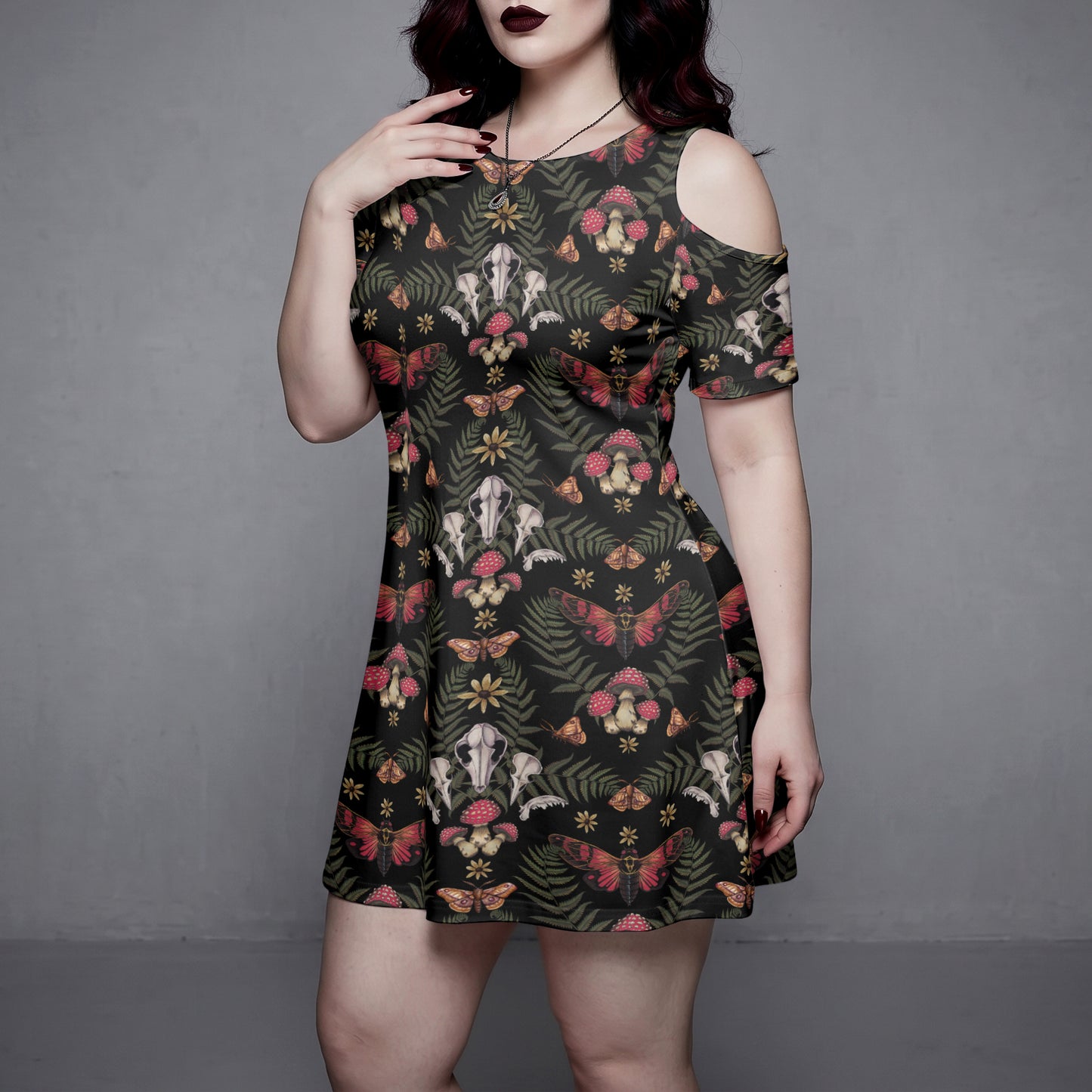 plus sized goth Woman wearing a witchy forest patterned dress against a gray background
