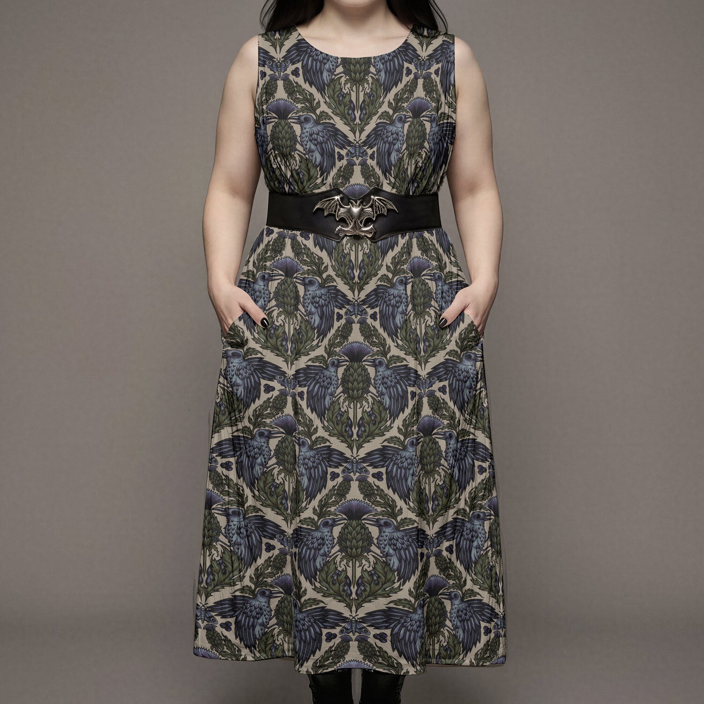 plus sized goth woman wearing a witchy raven thistle patterned dress with a belt on a plain background