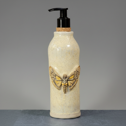 Ceramic bottle with moth design and pump on a gray background