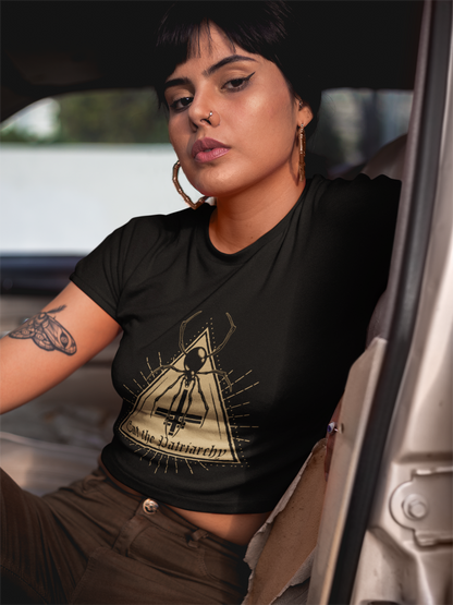 Woman with tattoos wearing a black eat the patriarchy t-shirt with a witchy graphic design, sitting inside a vehicle.