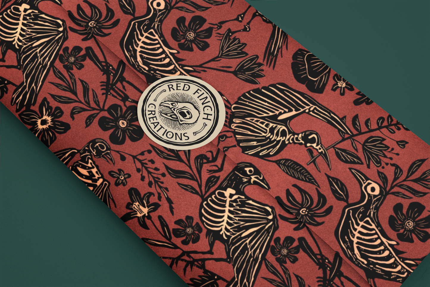 witchy wrapping paper with red background and black skeleton-like bird and floral pattern, featuring 'Red Finch Creations' logo.