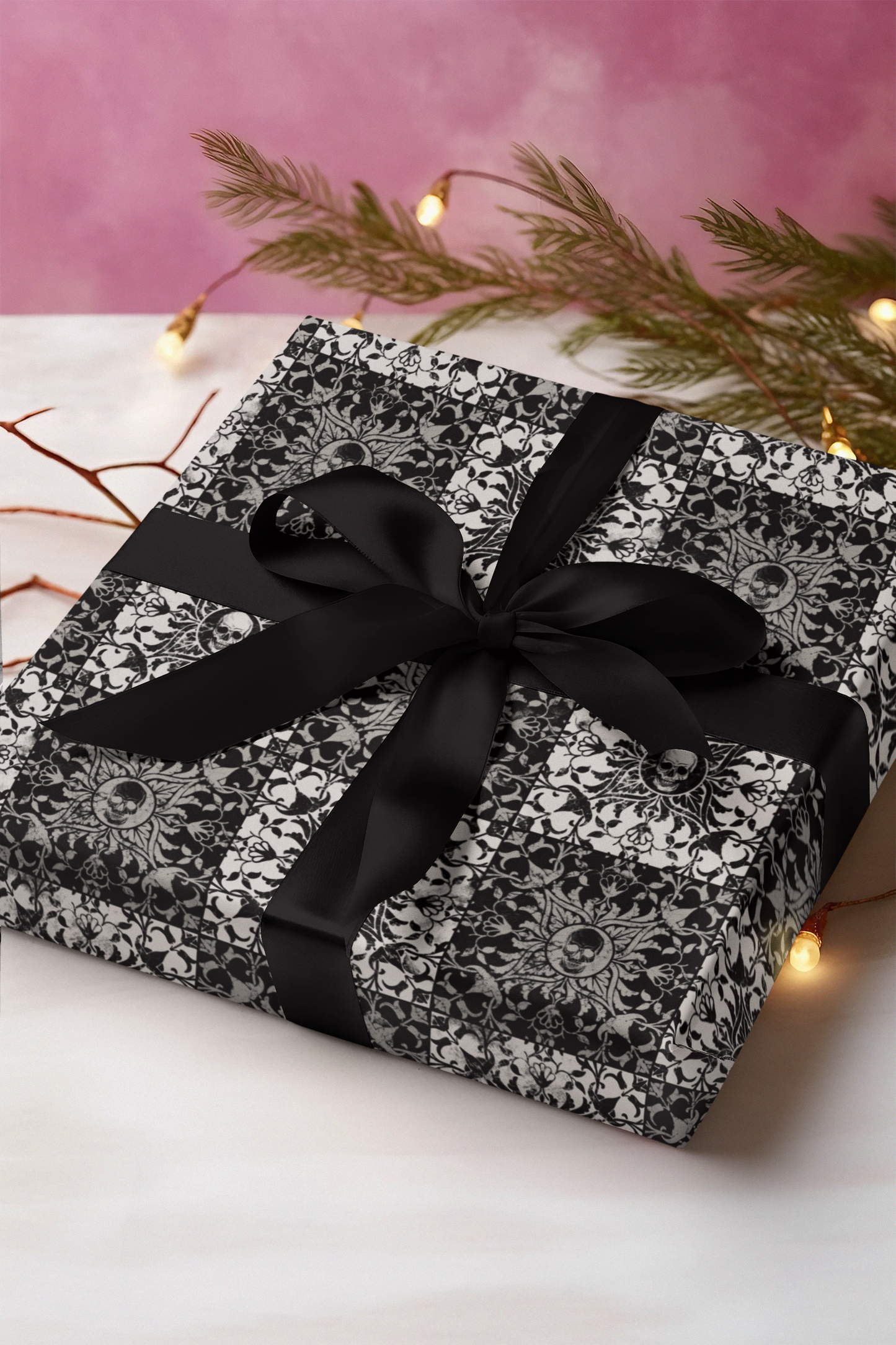 Gift box with black and white spooky skull pattern and black ribbon on a pink background with decorative lights and branches.