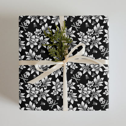 Gift wrapped in black and white floral and skull patterned paper with a green plant on a light gray background