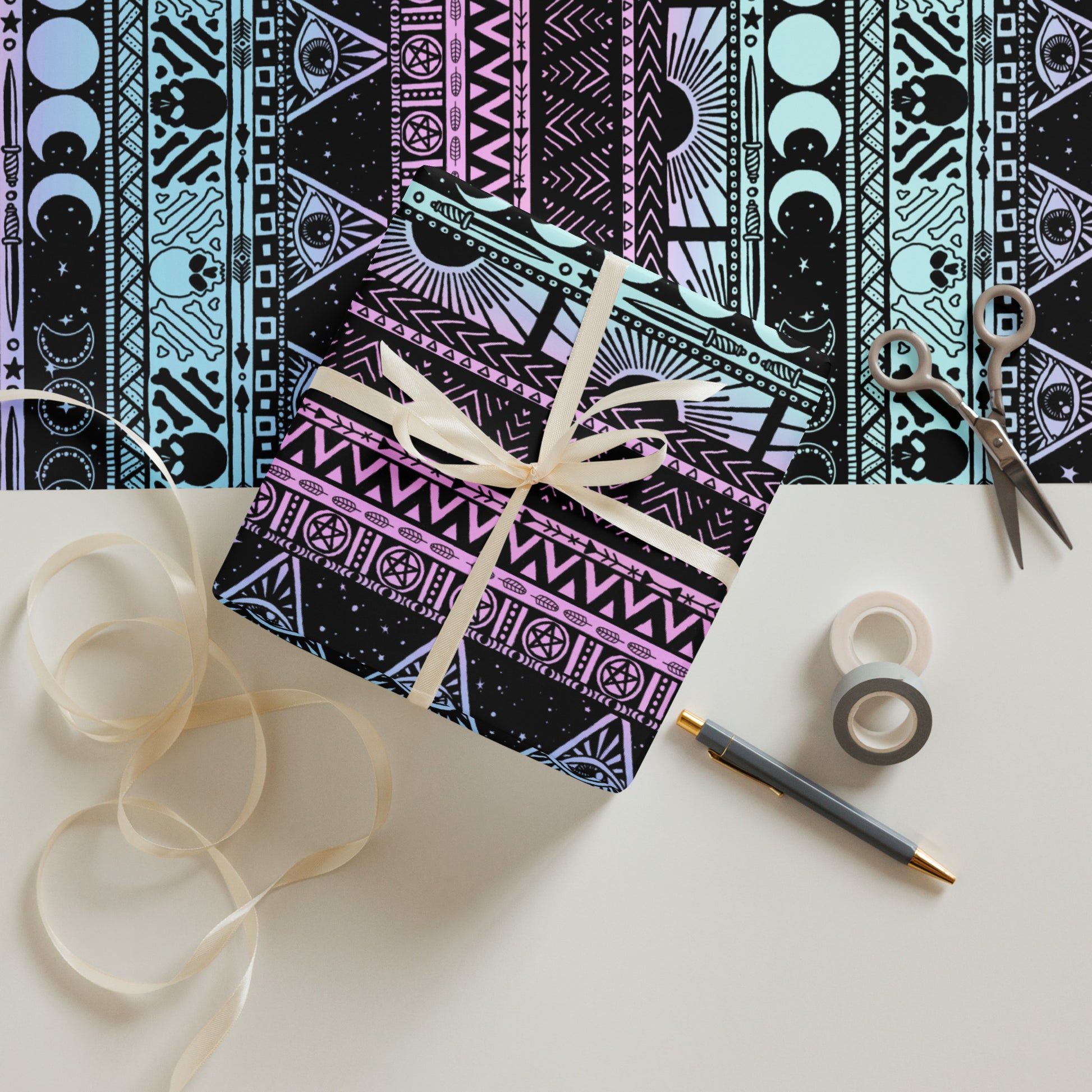 Decorative box with a witchy pastel patterned design, ribbon, scissors, and tape on a white surface.