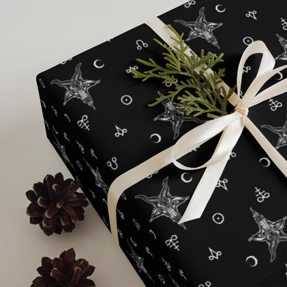 Gift box wrapped in black paper with satanic baphomet patterns, tied with a white ribbon, on a light background.