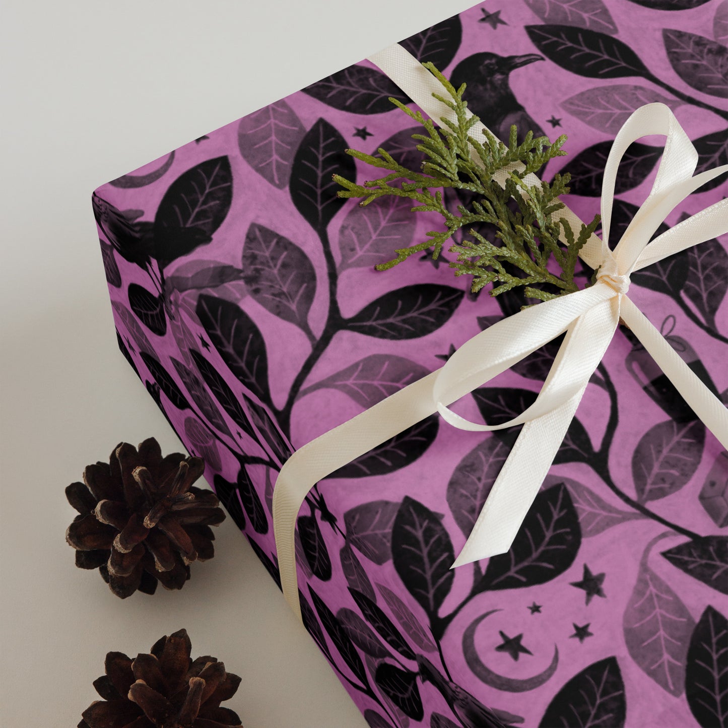 Gift wrapped in pink paper with black raven and leaf pattern, tied with white ribbon, on a light background.