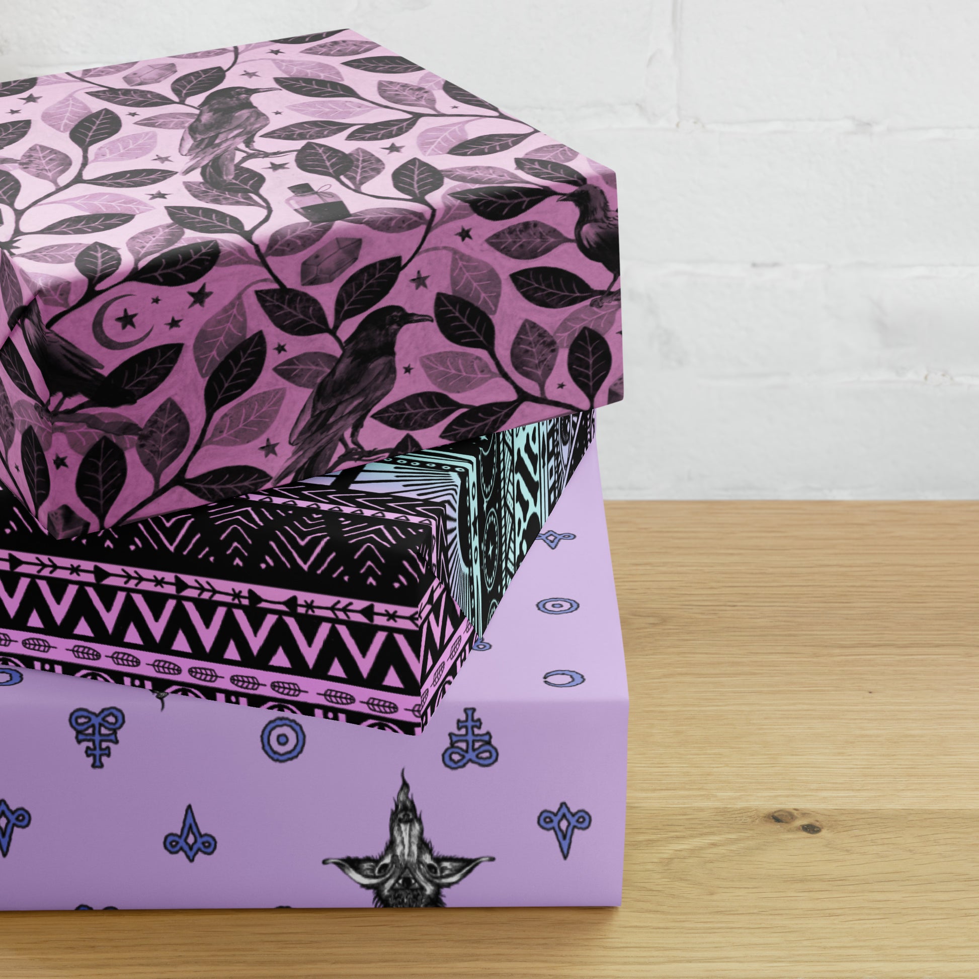 three boxes wrapped in pink gothic wrapping paper stacked on a wooden surface with a white brick wall background.