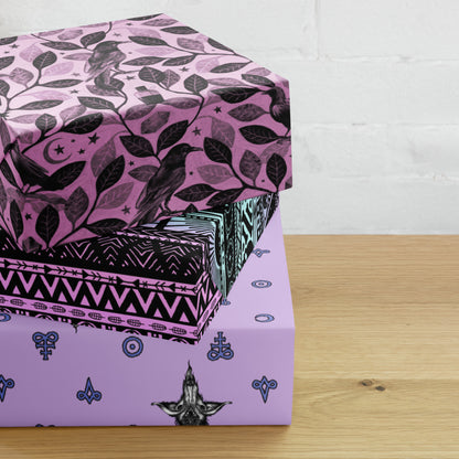 three boxes wrapped in pink gothic wrapping paper stacked on a wooden surface with a white brick wall background.
