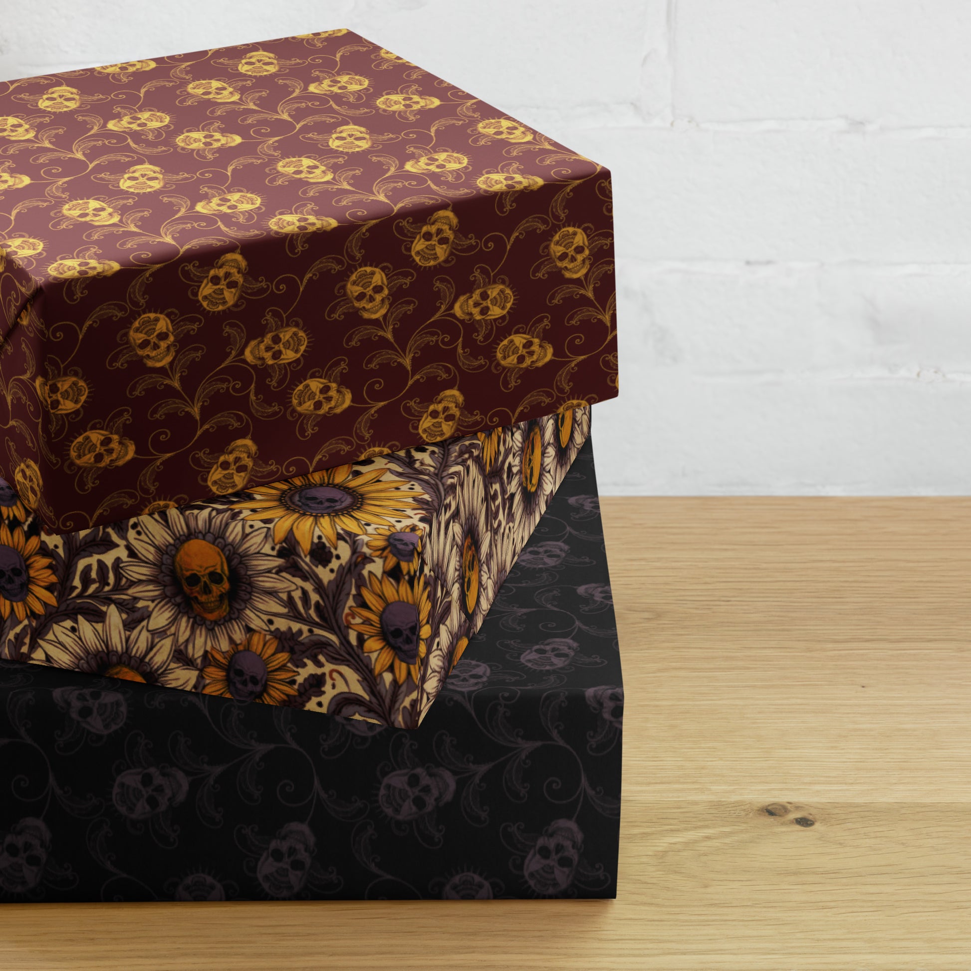 Three gift boxes with skull and floral-patterned gift wrap on a wooden surface.